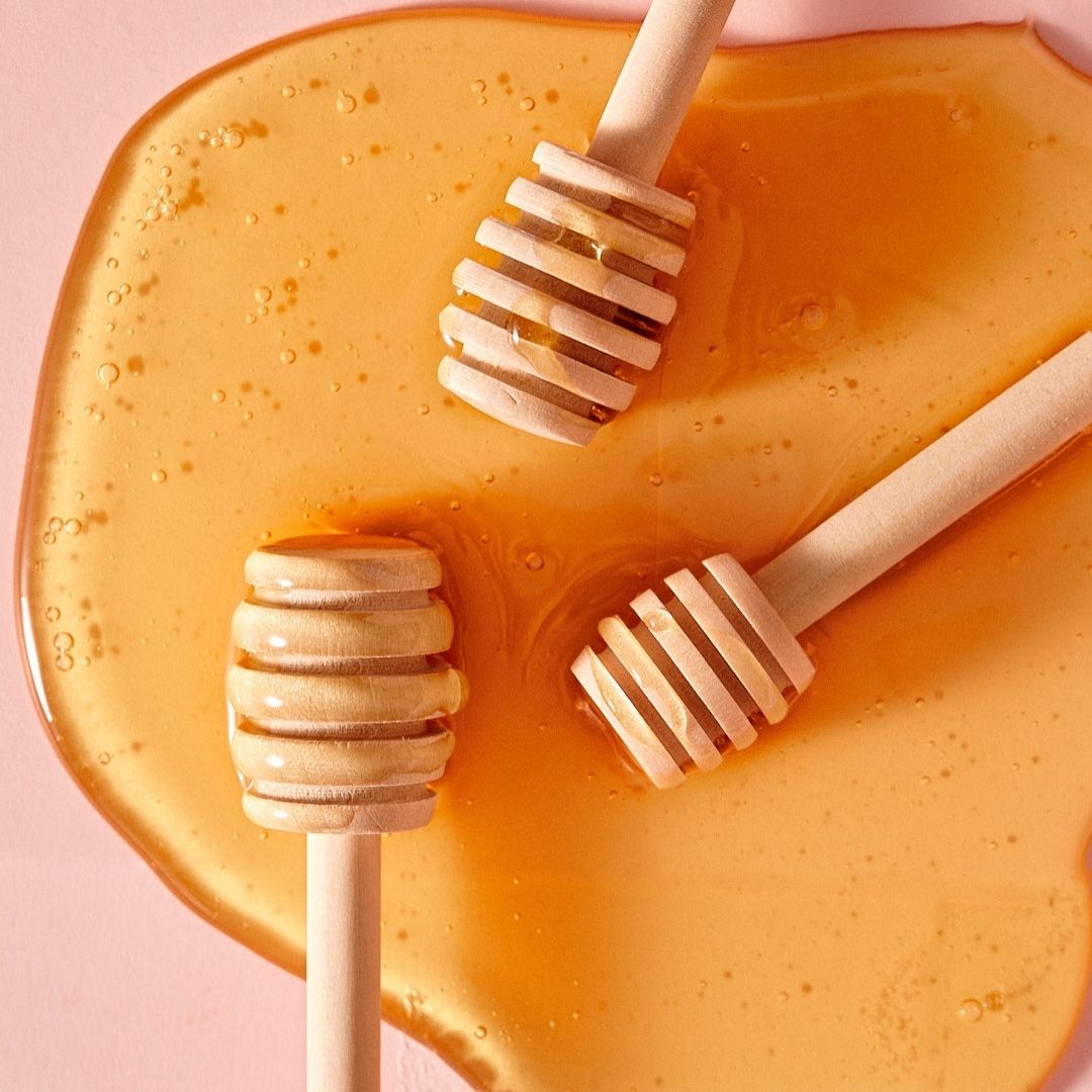 Three honey mixers in a puddle of honey on a pink background