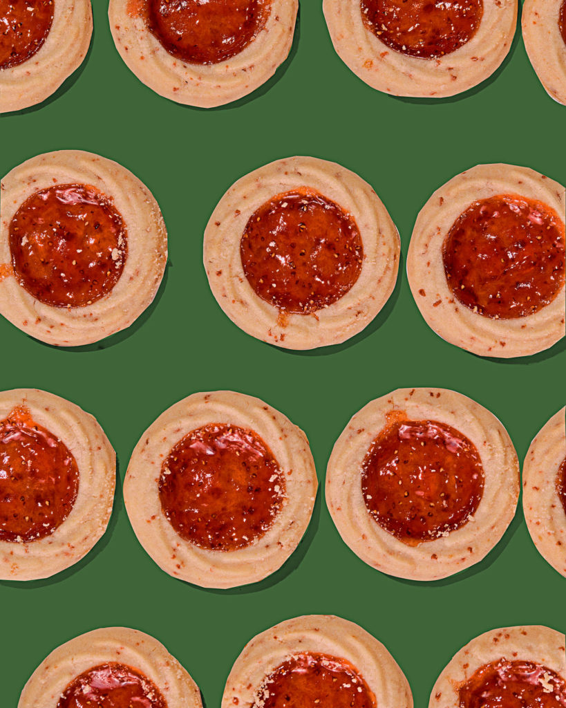 Strawberry linzer cookies placed in a row on a green background