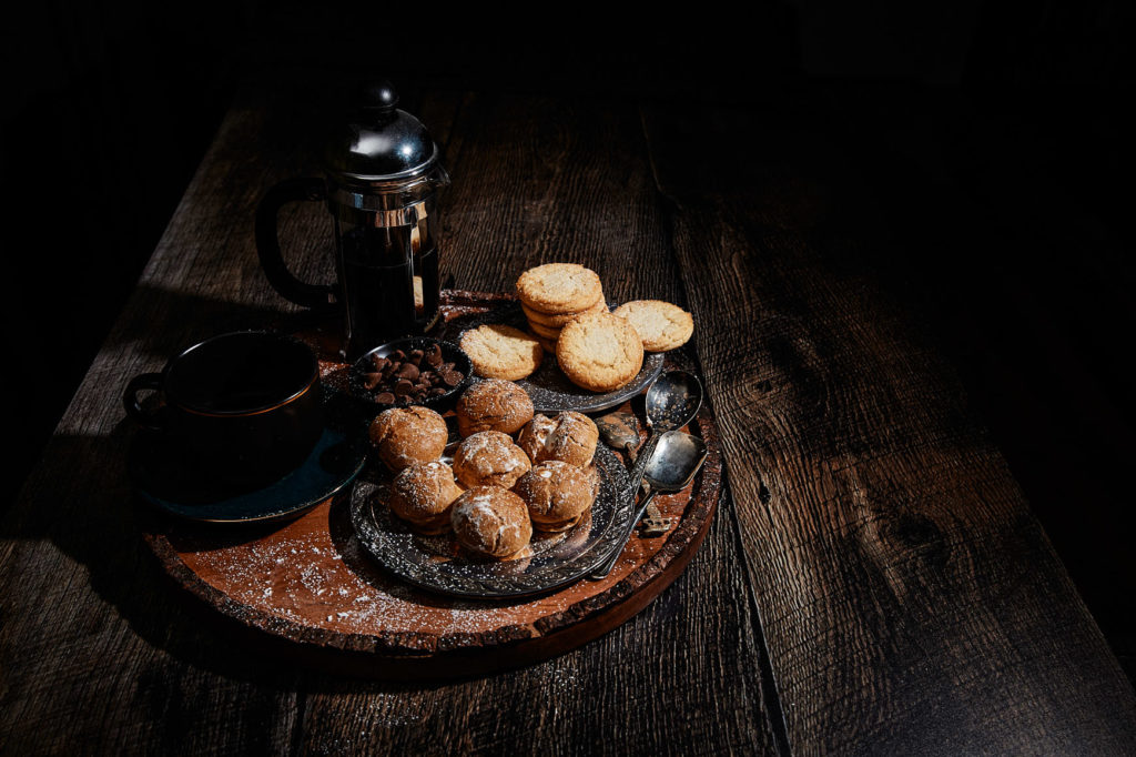Platter of creme puffs and coffee on a dark wooden table.