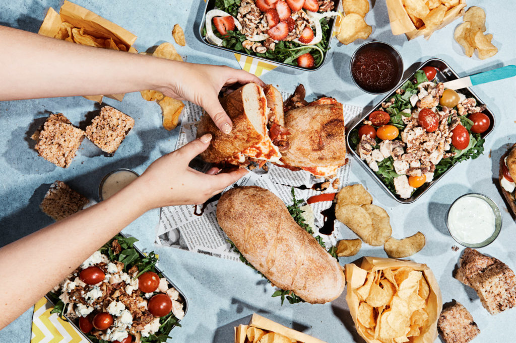 Flat lay of hands holding sandwiches and salads.