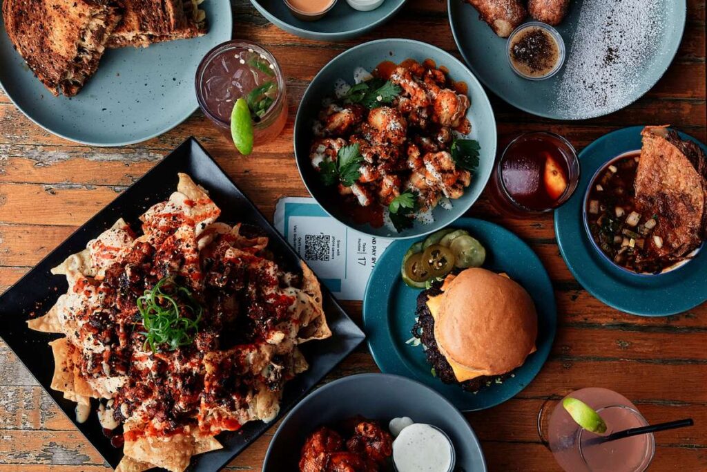 Overhead view of a mouth-watering spread featuring a juicy burger, crispy nachos, and golden cauliflower bites on a rustic wooden table at Lavaca Street Bar Restaurant.