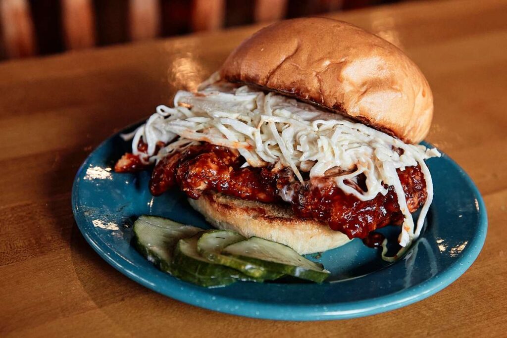 Delicious buffalo chicken sandwich accompanied by tangy coleslaw on a rustic wooden table.
