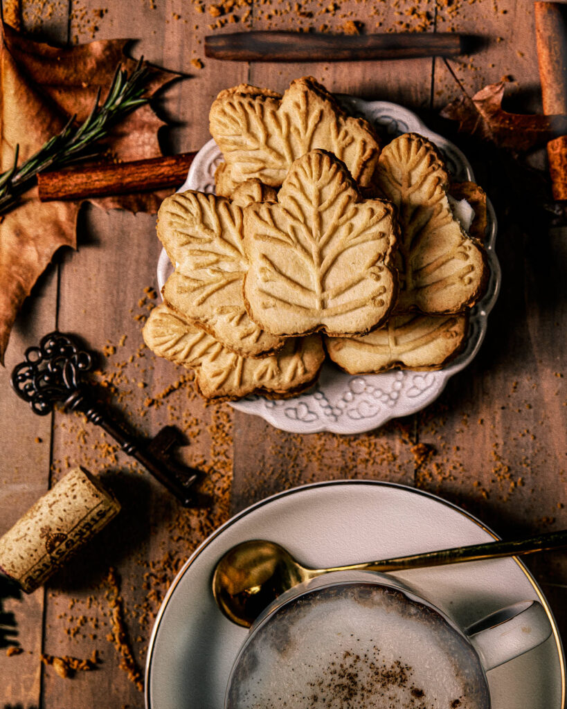 Festive maple tree cookies arranged on a vintage plate, surrounded by autumn leaves and a steaming cup of chai, showcasing the warm essence of the holidays.
